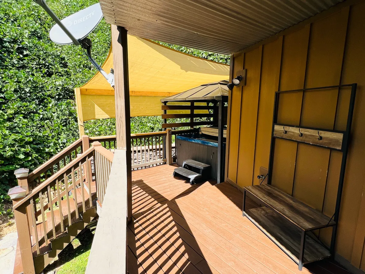 An exterior view of a deck with an outdoor seating area and a hot tub under a canopy. The inviting atmosphere is perfect for sunset views, outdoor dining, or stargazing, with the surrounding trees providing privacy and a strong natural connection.