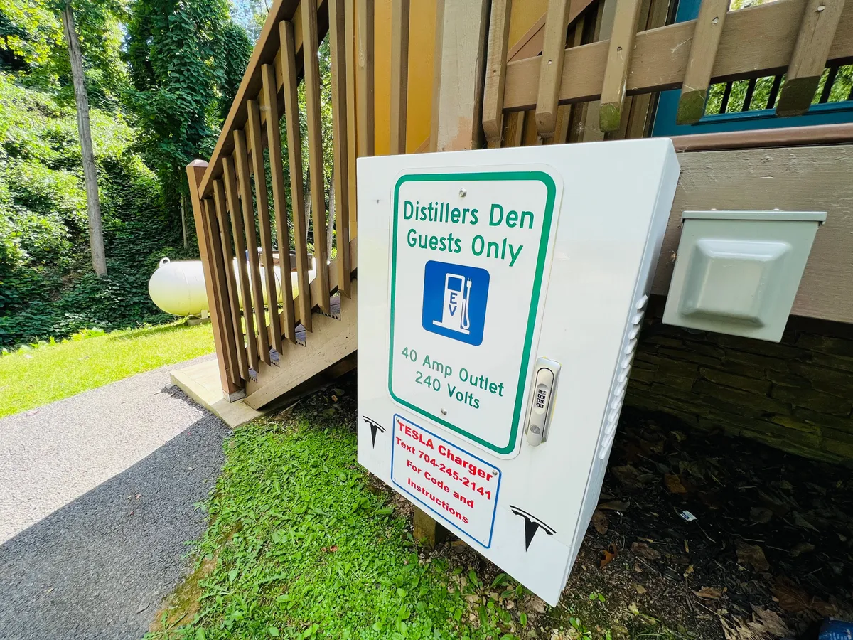 This image shows a modern charging station sign positioned near stairs, surrounded by lush greenery. The area exudes a sense of welcome and modern convenience, emphasizing the presence of electric vehicle amenities right at the property’s entrance. The natural surroundings hint at easy access to nature.