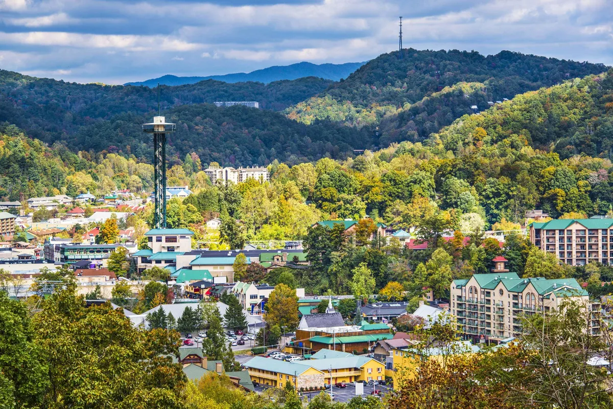 A wide view over the Gatlinburg townscape, framed by majestic mountains, with visible towers and treetops. The cheerful atmosphere captures the appeal of sightseeing and outdoor adventure.
