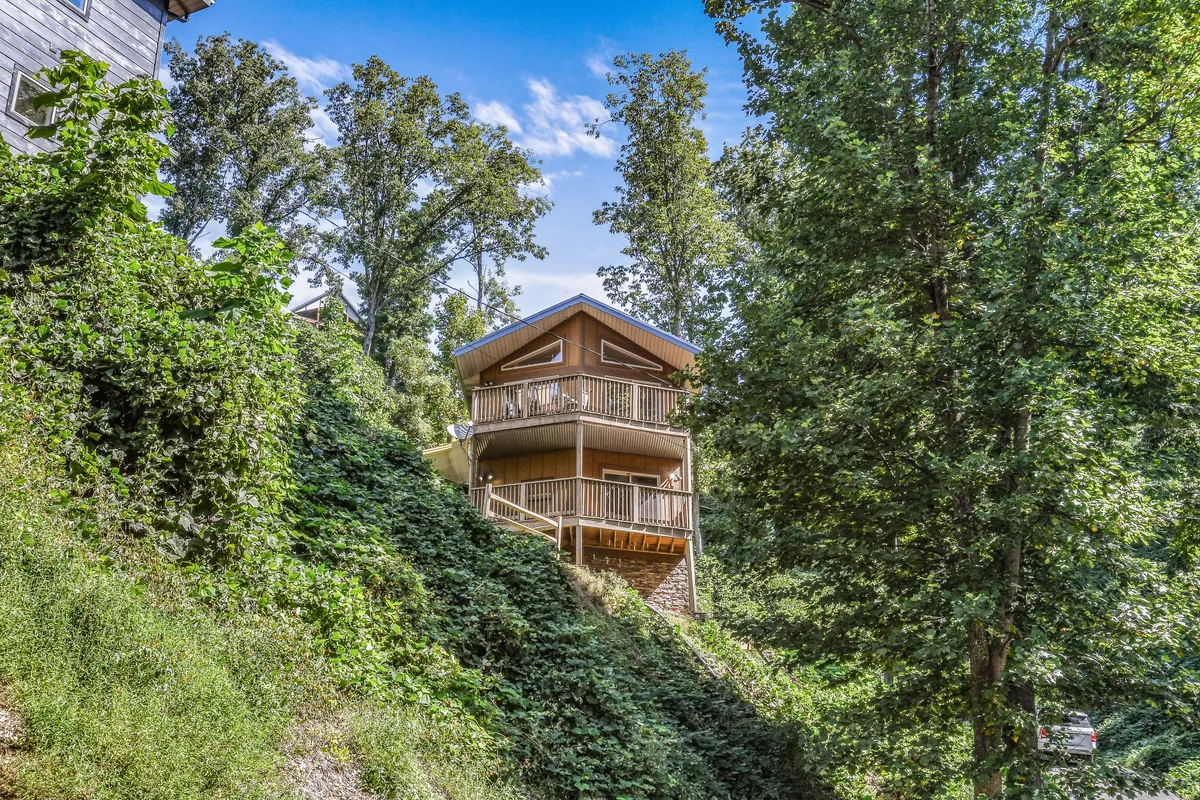 A three-story house surrounded by trees with a balcony perfect for socializing or taking in nature. The tranquil setting shows the cabin as a welcoming home base for group trips with seamless access to the lush surroundings.