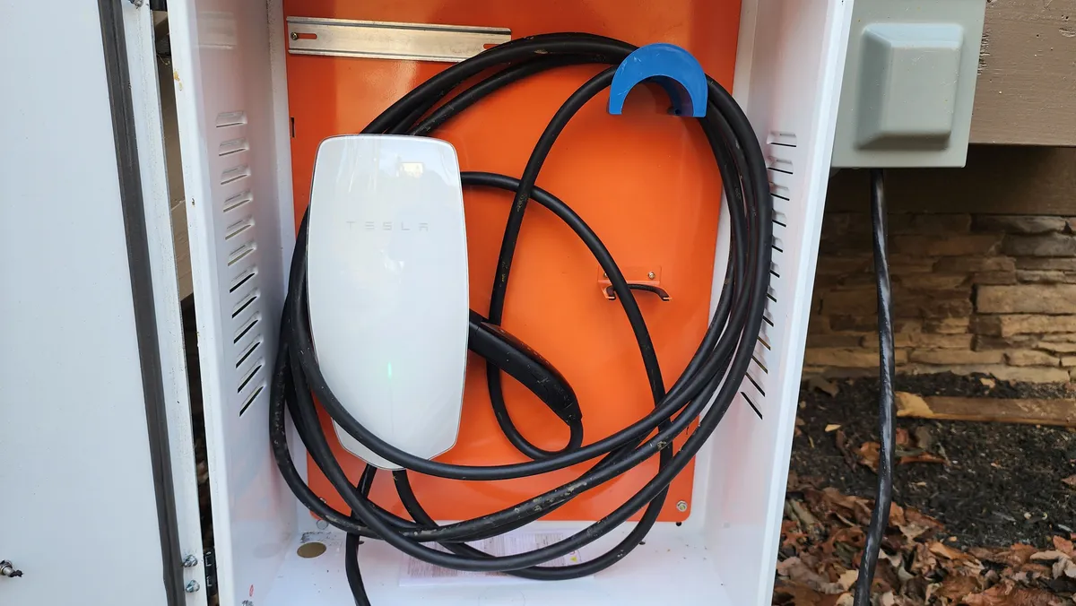 A close-up of a Tesla charging station with its orange interior box and coiled cable, highlighting the property's modern, eco-friendly amenities. The clean setup ensures easy access for electric vehicle travelers.