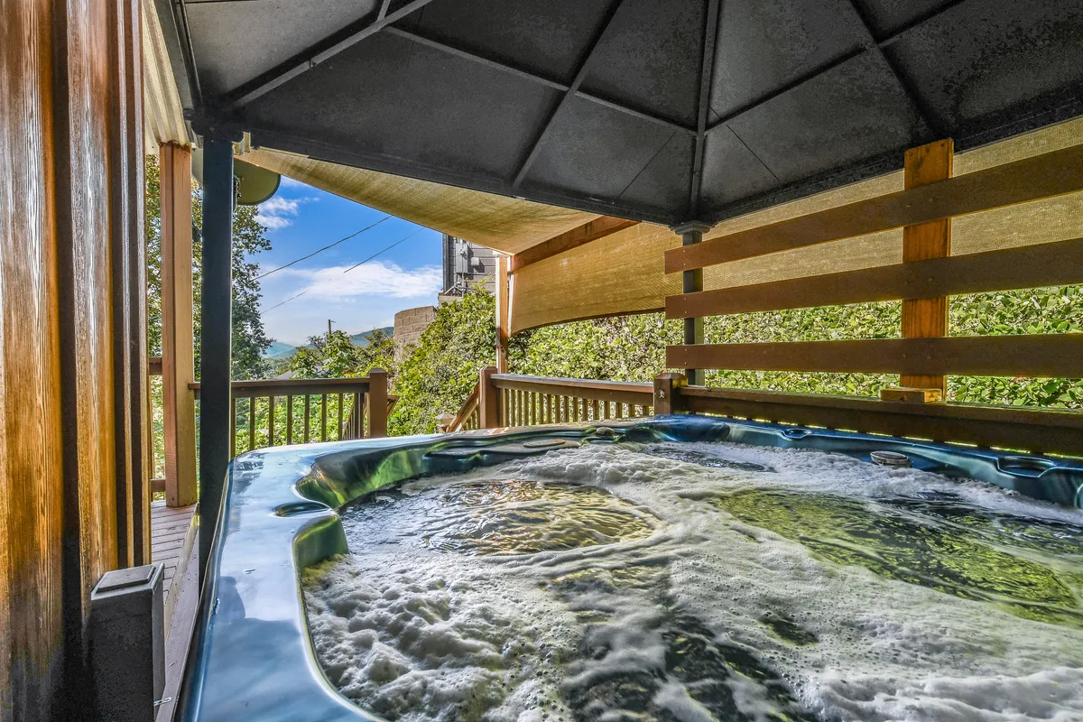 This image features a hot tub set on a wooden deck, surrounded by lush greenery and framed by a sturdy deck railing. The tranquil scene invites guests to relax in the warm water while soaking in the natural beauty of the Great Smoky Mountains.