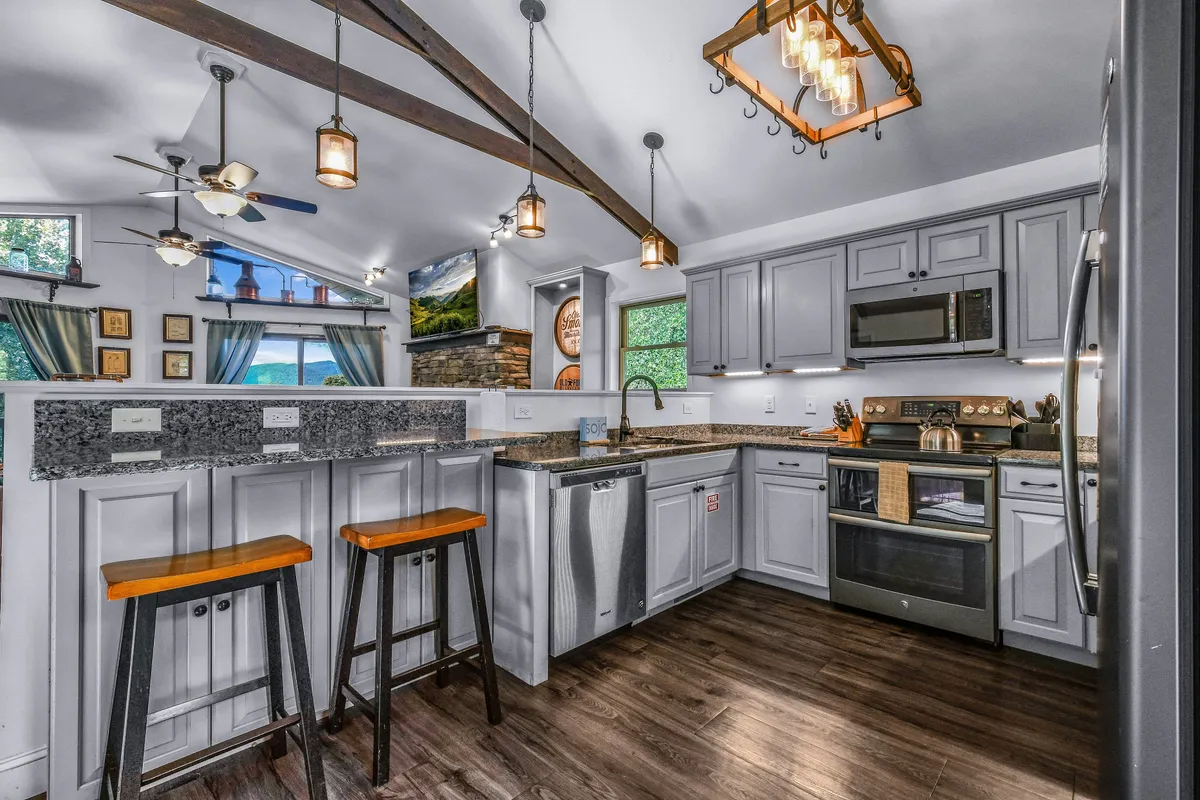 The kitchen area features a granite countertop island with seating, exposed ceiling beams, and stylish hanging light fixtures. The setup is perfect for casual breakfasts or preparing festive dinners, all while remaining connected to the main living space.