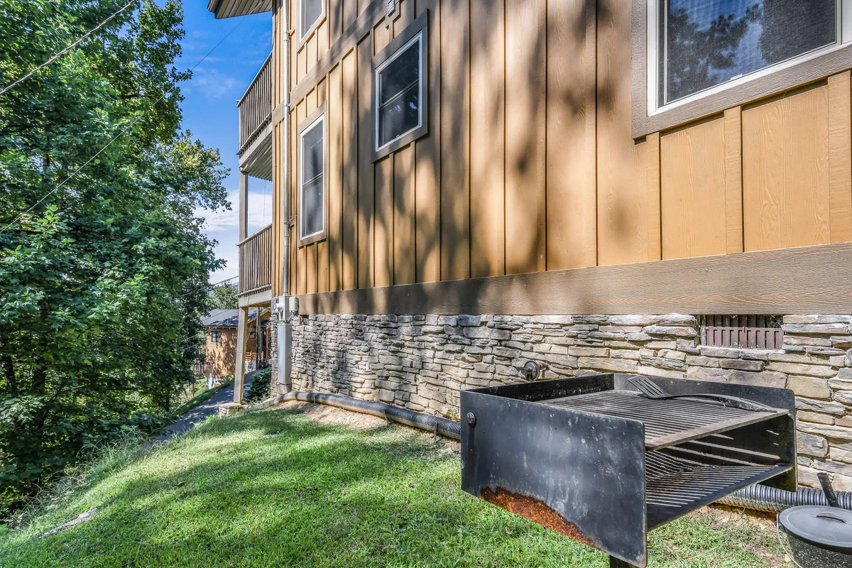 This image centers on a charcoal grill positioned beside a stone foundation, with grassy areas and trees in the background. It's an ideal spot for preparing memorable dinners in a relaxed, natural setting.