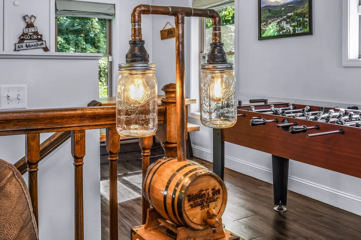A relaxed corner of the play loft, showing a foosball table beneath a unique light fixture and adjacent to a rustic wooden barrel. The mood is casual and fun, ideal for socializing and hosting game nights with friends or family.